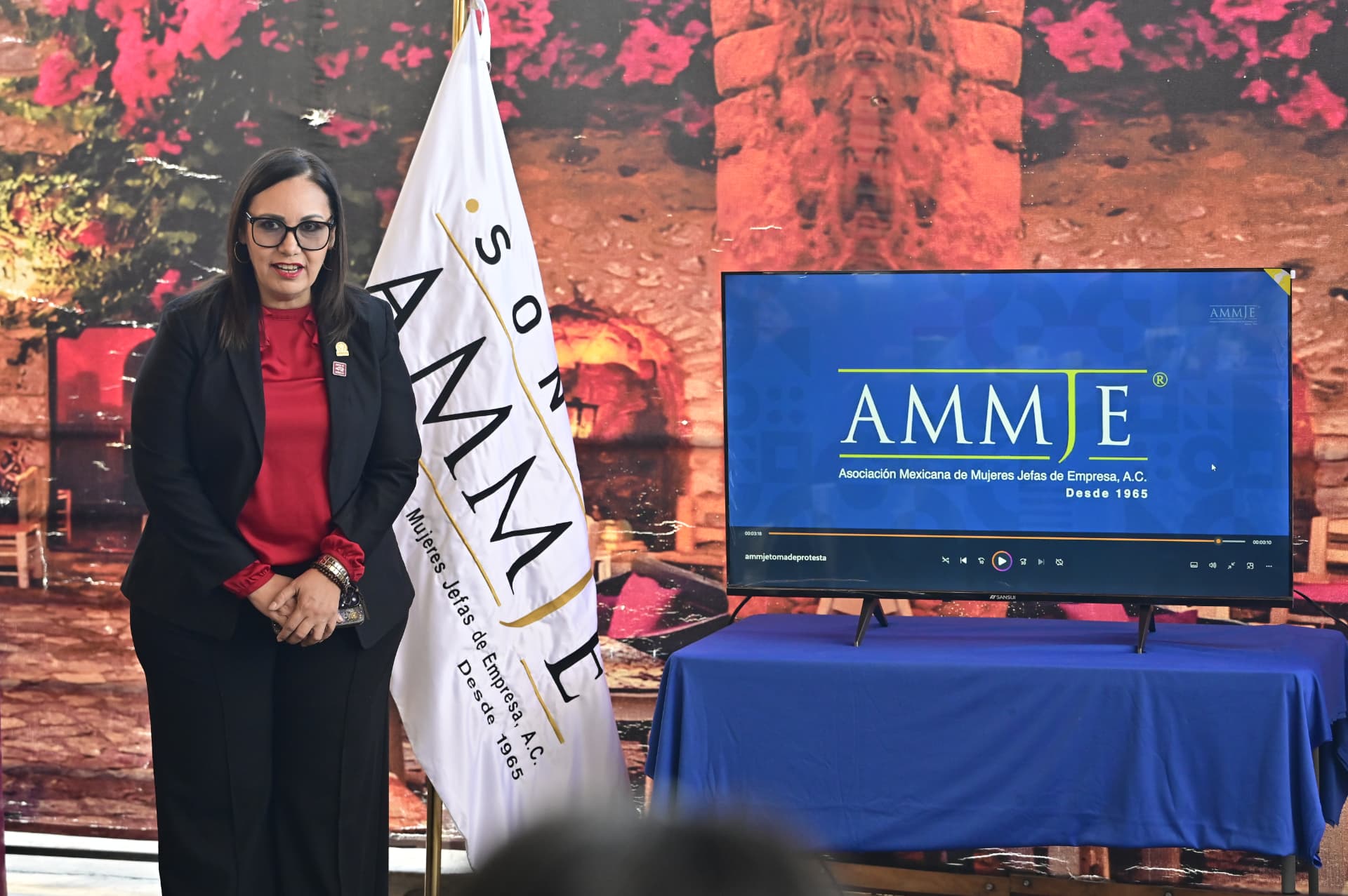 La presidenta de AMMJE Sonora junto al lábaro de la asociación durante el desayuno empresarial de febrero de 2026